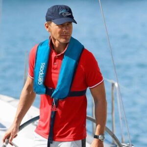 Compass Compact II 150N Rettungsweste in royal blau auf einem Segelboot getragen von einem Mann im roten T-Shirt, ideal für Sicherheit und Komfort beim Wassersport.