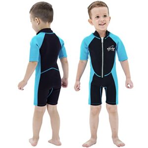 Glückliches Kind trägt einen blau-schwarzen 2,5 mm Neoprenanzug am Strand, ideal für schwimmende Aktivitäten und UV-Schutz.