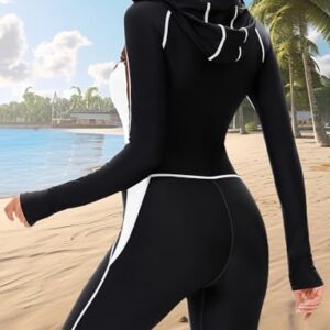 Frau im Tauchanzug auf der Strandpromenade. Der Tauchanzug ist braun und hat eine Kapuze. Der Strand ist sandig mit Palmen in der Hintergrund unter blauem Himmel.